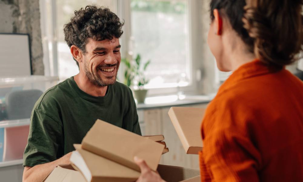 young couple smiling while packing for a move, to show "downsizing to an apartment" from Anderson Communities